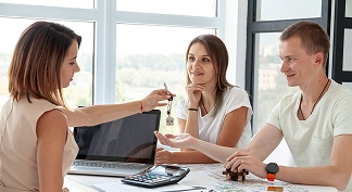 Bir çift, masada danışmanla sözleşme imzalarken evin anahtarlarını alıyor.