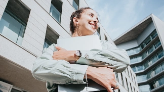 Yeni taşındıktan sonra modern bir apartmanın önünde belgelerini elinde tutan ve gülümseyen mutlu bir kadın.