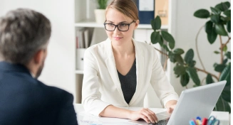 Modern bir ofis ortamında, müşteriyle yaptığı toplantı sırasında dizüstü bilgisayarında çalışan profesyonel bir iş kadını.